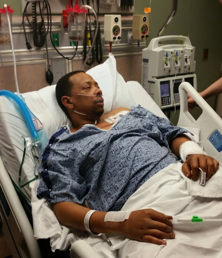 A man resting in a hospital bed with oxygen and monitors beside him