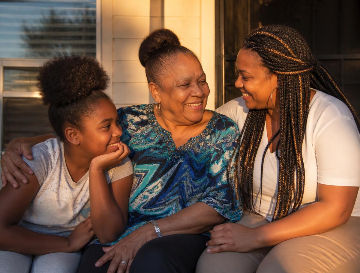 Three generations of a Black family sitting together on a Memphis front porch at golden hour