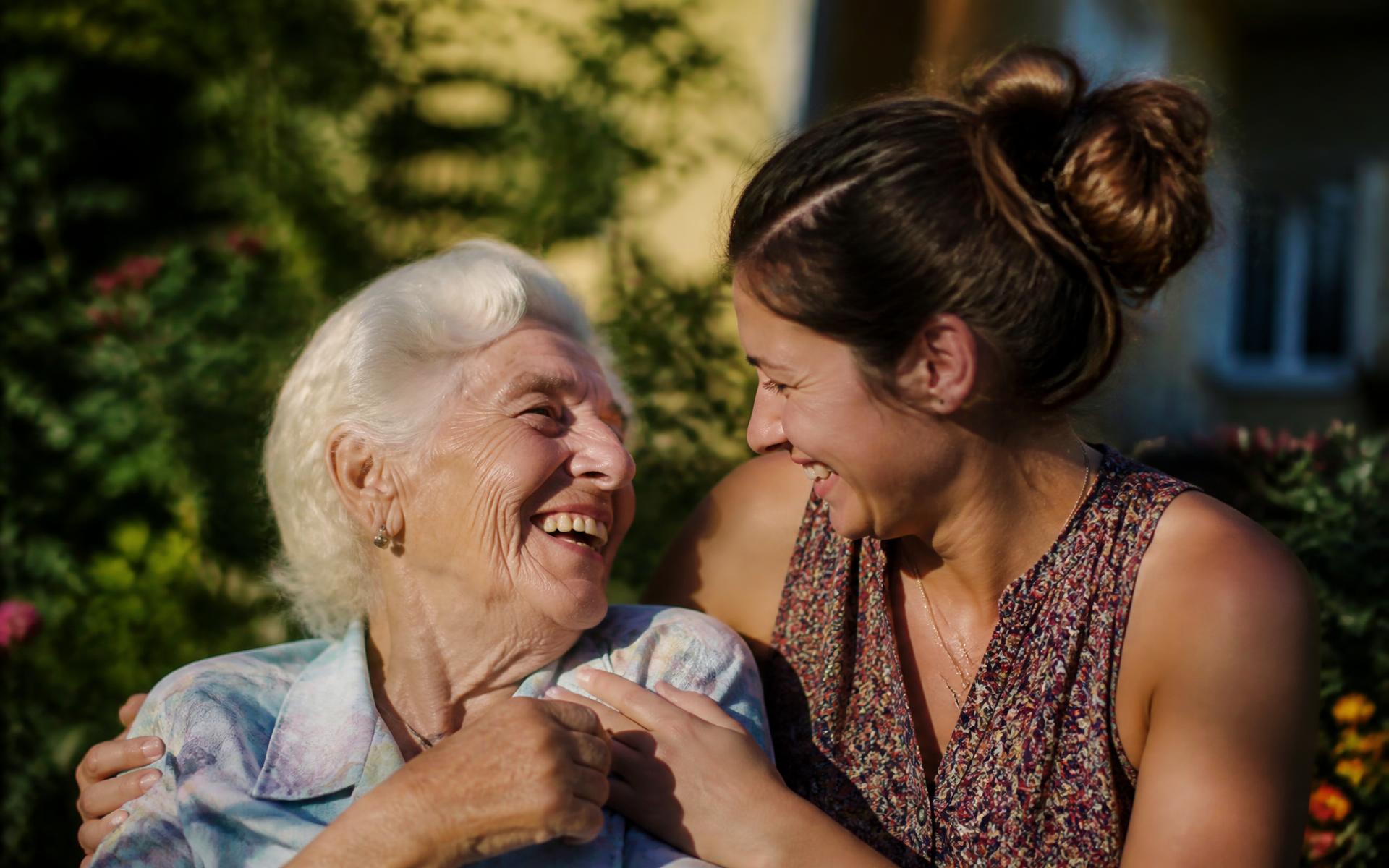 A grandmother and her granddaughter share laughter in a sunlit garden
